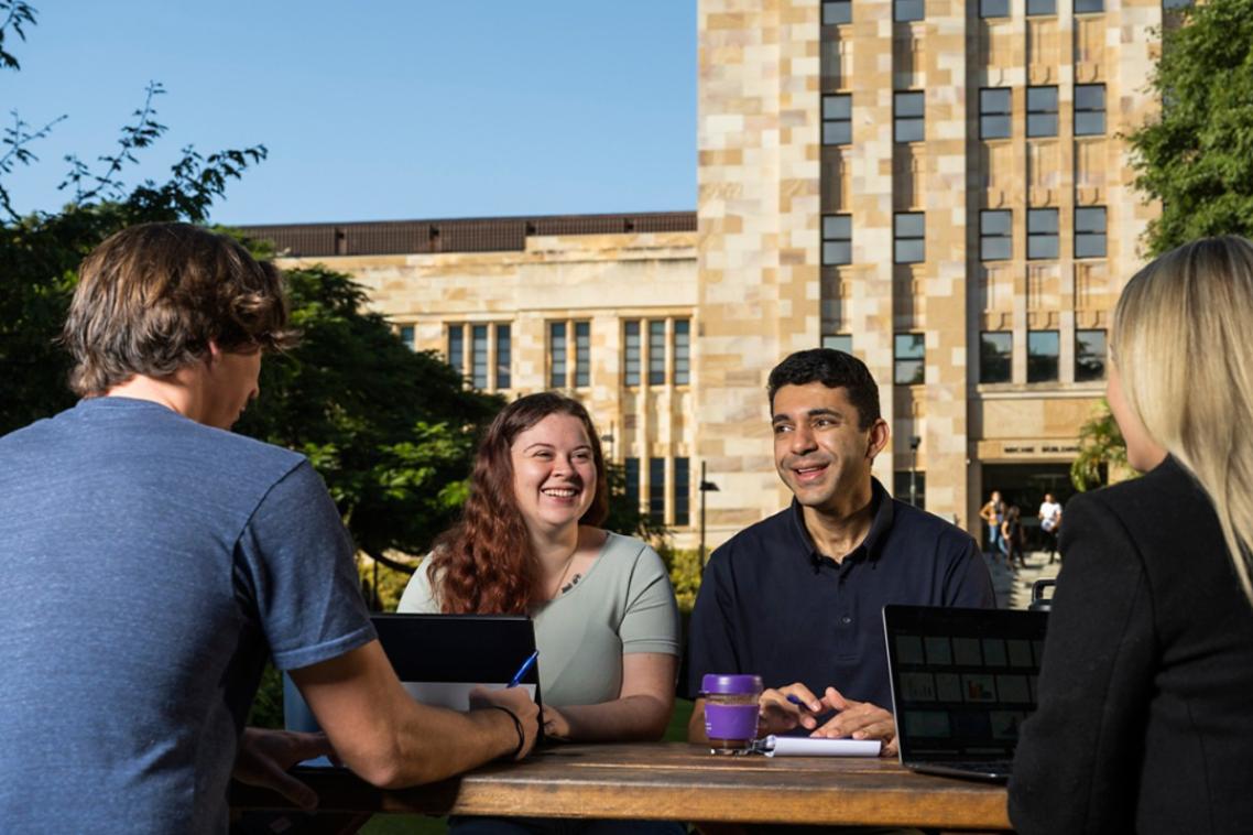 A group of students sitting at a table in front of a sandstone building