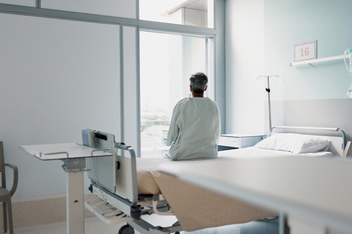 A patient sitting on a bed in a hospital room and looking out the window.